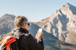 © ADDICTIVE STOCK - Senior traveling woman browsing on mobile phone on mountains