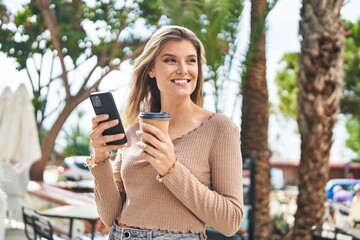 Poster - Young blonde woman using smartphone drinking coffee at street