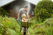 © Maria Sbytova - Happy little boy having fun in a wheelbarrow pushing by dad in domestic garden on warm sunny day. Child watering plants from a hose. Active outdoors games for kids in summer.