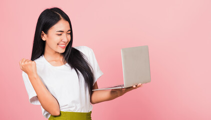 Poster - Portrait of happy Asian beautiful young woman teen confident smiling face holding using laptop computer and excited celebrating success, studio shot isolated on pink background, with copy space