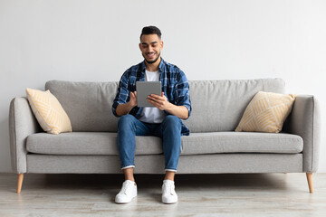 Wall Mural - Smiling young Arab man using digital tablet at home