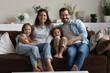 © fizkes - Happy homeowners well-being family portrait, bank loan and medical insurance cover concept. Beautiful couple and two preschool children sitting on cozy sofa in living room smiling looking at camera