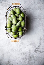 An Overhead View Of A Basket Of Freshly Picked Feijoa Fruit On A Distressed Background