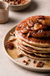 © The Picture Pantry - A plate of maple pecan pancakes with caramelized bananas on a table with a platter of pancakes and syrup in the background.