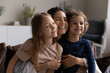 © fizkes - Loving young woman cuddling her preschool son and daughter, family smiling looking aside sit on sofa in living room, close up view. Concept of happy motherhood, unconditional mothers love, adoption