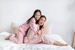 Cheerful asian young girl hugging millennial woman in pink pajamas sitting on bed have fun in bedroom