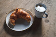 fresh golden brown croissant with a cappuccino on a stoneware plate and rustic wooden table