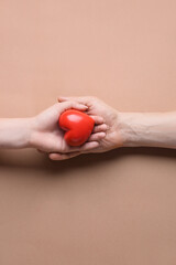 Wall Mural - Female and male hands with red heart on color background. Donation concept