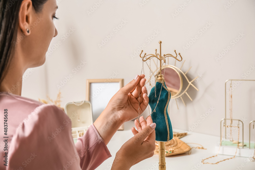 Woman taking stylish necklace from stand on white table