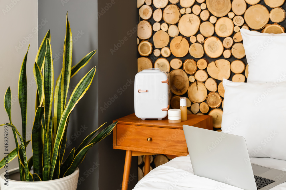 Small cosmetic refrigerator on bedside table near wooden wall
