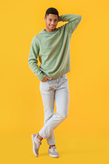 Wall Mural - Handsome African-American guy in knitted sweater on yellow background
