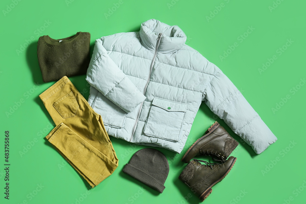 Winter jacket, sweater, pants, hat and shoes on green background
