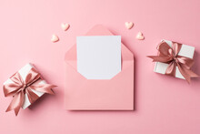 Top View Photo Of Valentine's Day Decorations Open Pink Envelope With Paper Sheet Two Small White Gift Boxes With Pink Bows And Hearts On Isolated Pastel Pink Background With Empty Space