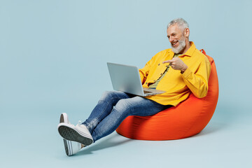 Sticker - Full body smiling fun elderly gray-haired mustache bearded man 50s wear yellow shirt sit in bag chair hold use work point on laptop pc computer isolated on plain pastel light blue background studio