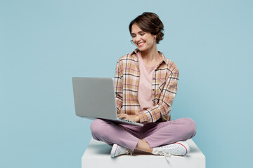 Wall Mural - Full body young smiling copywriter happy cool woman 20s in brown shirt sit on white chair hold use work on laptop pc computer isolated on pastel plain light blue b ackground People lifestyle concept