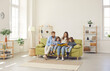 © Studio Romantic - Happy family spending time at home. Mum, dad and little kids reading book while sitting together on green sofa in room with light walls, beige rug and simple brown shelves in their big new house