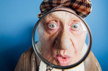 Wall Mural - Funny portraits with old grandmother. Senior woman acting as an investigator with the magnifying lense
