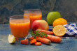 Natural organic fresh juice made of carrots and apples on blue background. Healthy carrot, apple and lemon smoothie.