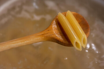 two noodles on a wooden spoon over a pot of water