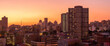 A horizontal panoramic cityscape taken after sunset, against a pink and orange sky, of the central business district of the city of Johannesburg, South Africa