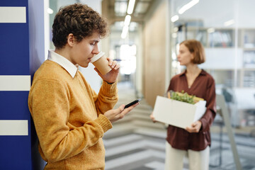 Wall Mural - Side view portrait of young employees on break in office focus on man drinking coffee in background, copy space