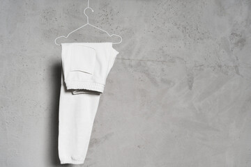Wall Mural - Blank white sweatpants hanging on the thin metallic hanger against light concrete wall