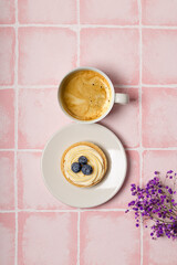 Wall Mural -  Cup of coffee, cake and violet flowers on pink background top view, vertical photo. Greeting card for women day