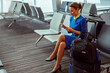 Woman stewardess in air hostess uniform sitting on chair and holding smartphone while waiting for flight in departure lounge
