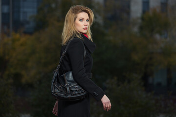 Wall Mural - Young woman in black coat with leather handbag