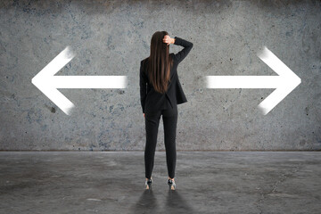 Wall Mural - Back view of businesswoman with two arrows in concrete interior. Different direction and choice concept.