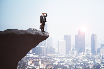 Canvas Print - Handsome young european male on cliff edge looking into the distance on bright city background with daylight and mock up place. Future, success, leadership and career growth concept.