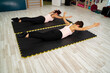 Two young beautiful women in gym laying on yoga mat with arms and legs raised, strengthening core part of the body and abs. Core exercises 