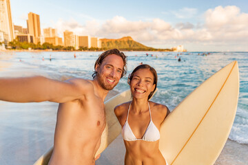 Wall Mural - Hawaii beach selfie happy couple surfers smiling to camera taking phone photo at surfing lesson in Waikiki, Honolulu city, Oahu island, Hawaii, USA. Asian bikini woman holding surfboard on vacation