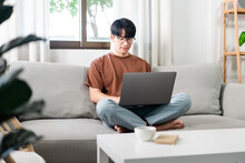 Technology Concept The Male Who Is Wearing Casual Clothes Sitting On The Sofa, Resting His Notebook On His Lap And Doing His Work