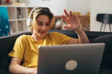 teenage boy with sitting on a sofa and using laptop computer at home for video chatting