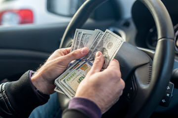 Wall Mural - hands holding dollar bills in the middle in the car interior on the steering wheel background