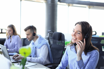 Wall Mural - Portrait of smiling female customer service agent wearing headset with colleagues working in background at office