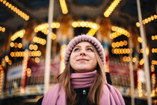 Smiling Young Woman Standing In Front Of Illuminated Carousel