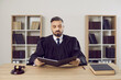 © Studio Romantic - Serious male judge reads legal documents on case sitting at table in his office. Portrait of middle aged man in mantle judge sitting near gavel and court book with folder of documents.