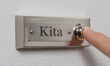 Person drückt Türklingel mit der Beschriftung Kita