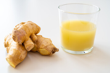 Ginger root, with pieces of ginger next to it and a glass of ginger juice. 