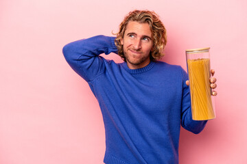 Wall Mural - Young caucasian man holding spaghettis jar isolated on pink background touching back of head, thinking and making a choice.