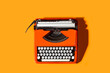 Máquina de escribir retro naranja de los años 60/70 sobre un fondo anaranjado. Vista superior. Copy space