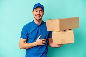 Wall Mural - Young delivery caucasian man isolated on blue background laughing and having fun.