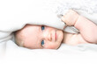 Little caucasian baby under white blanket. Small kid with blue eyes on light white background with copy space.