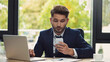 © LIGHTFIELD STUDIOS - young businessman looking at mobile phone while working at laptop in office