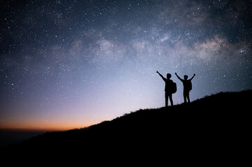 Wall Mural - Silhouette of two tourists standing and watched the star, milky way and beautiful view night sky on top of the mountain. They are enjoyed traveling and was successful when he reached the summit.