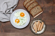 Plate with fried eggs, bread and susages on a wooden table.