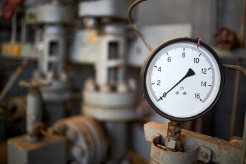 Pressure gauge or manometer shows zero closeup with crane or valve cover out of focus background with copyspace. Example of chemical plant retro style equipment.