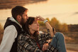 © Vagengeim - Candid portrait of two lovers at dusk. Couple sit on the ground and hug, greet the sunset together. Concept of youth, love and lifestyle. Authentic real people.